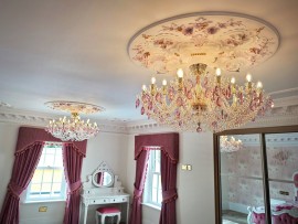 The chandeliers match the purple-red curtains at the window.