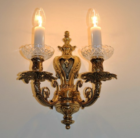 Golden wall light with two metal arms made of solid cast brass.